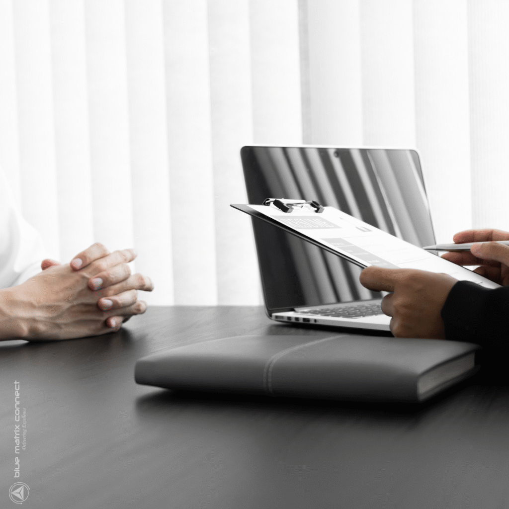 Photo of a person being interviewed. The interviewer holds a clipboard and has a document for discussion.