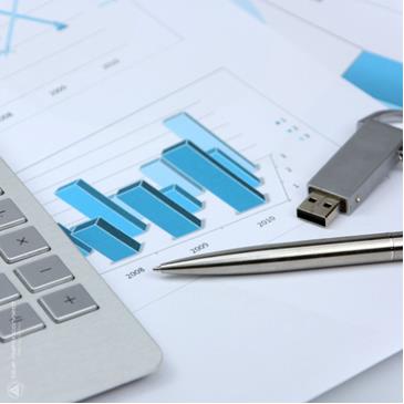Close-up of a printed bar chart with blue bars placed on a desk beside a laptop keyboard, USB drive, and pen.