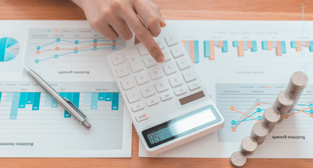 Business person using a calculator with financial charts and stacked coins on desk, representing compliance services, financial accuracy, and business growth
